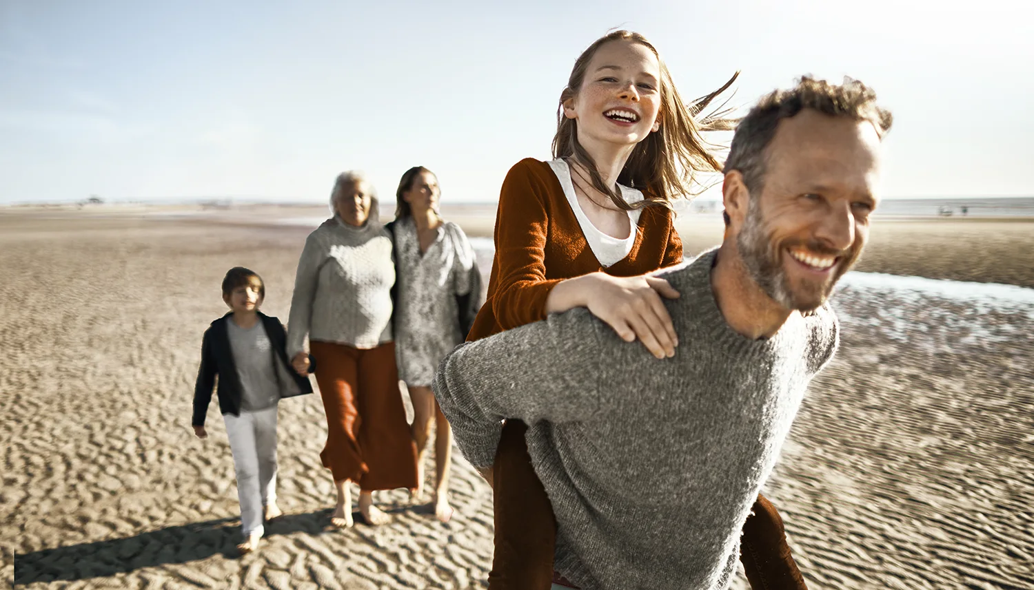Eine Familie macht einen Ausflug am Strand. Sie sehen glücklich aus. | VIACTIV Krankenkasse