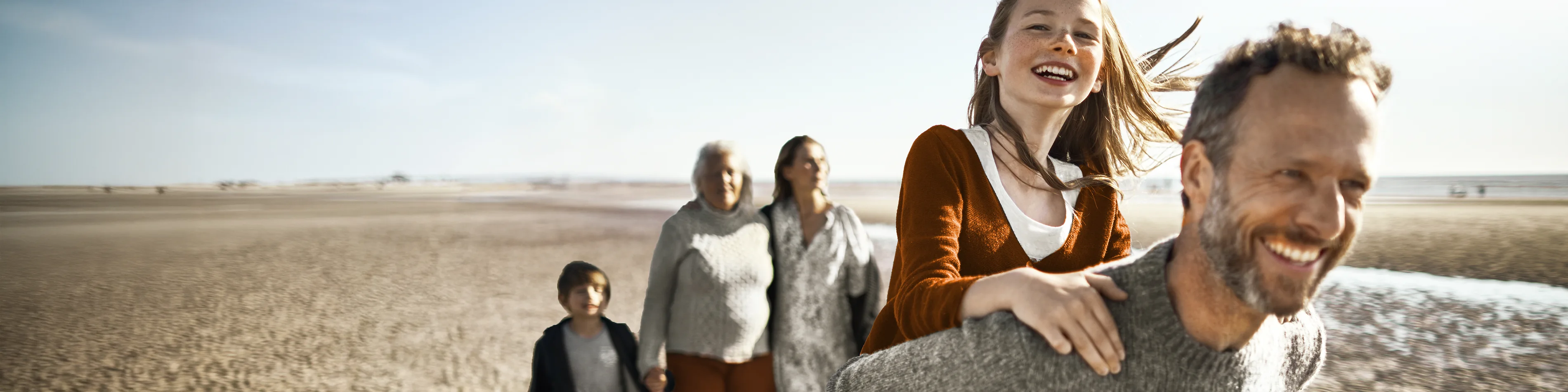 Eine Familie macht einen Ausflug am Strand. Sie sehen glücklich aus. | VIACTIV Krankenkasse