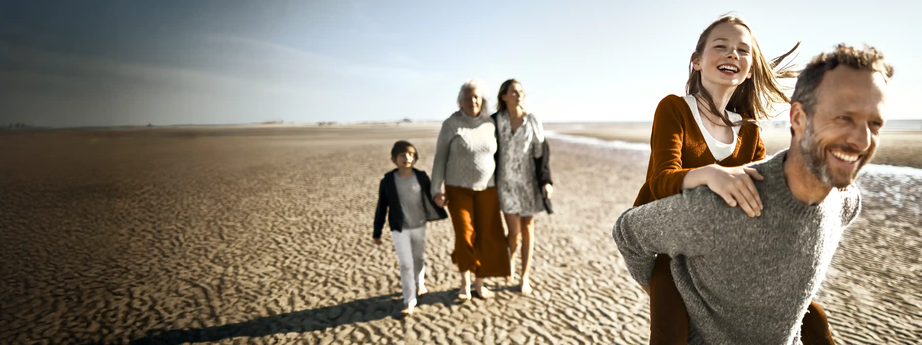 Eine Familie macht einen Ausflug am Strand. Sie sehen glücklich aus. | VIACTIV Krankenkasse