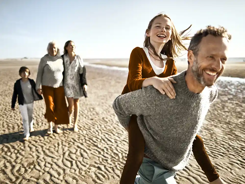 Eine Familie macht einen Ausflug am Strand. Sie sehen glücklich aus. | VIACTIV Krankenkasse