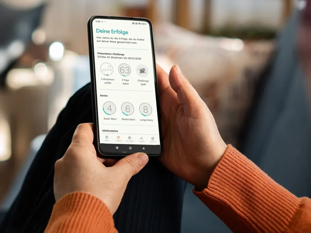 Eine Frau liegt sitzt auf dem Sofa und schaut sich über ihr Smartphone die Detoxi-App an. | VIACTIV Krankenkasse