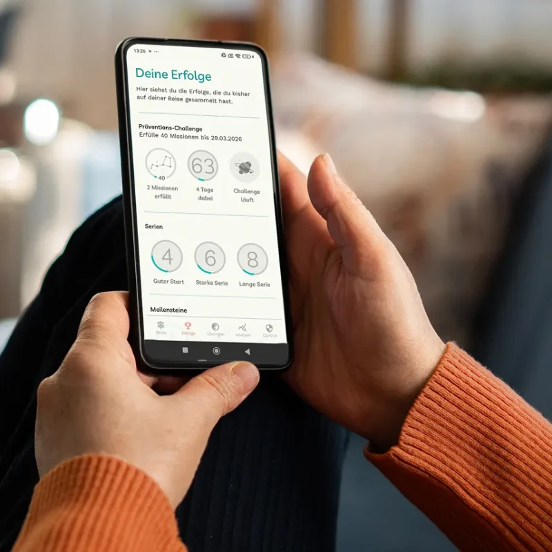 Eine Frau liegt sitzt auf dem Sofa und schaut sich über ihr Smartphone die Detoxi-App an. | VIACTIV Krankenkasse
