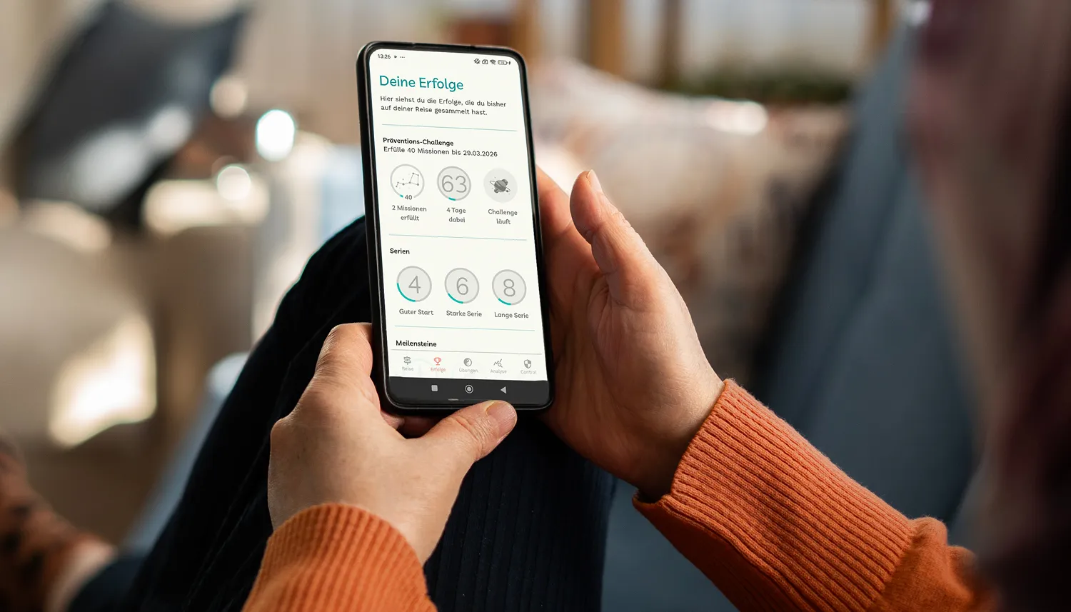 Eine Frau liegt sitzt auf dem Sofa und schaut sich über ihr Smartphone die Detoxi-App an. | VIACTIV Krankenkasse