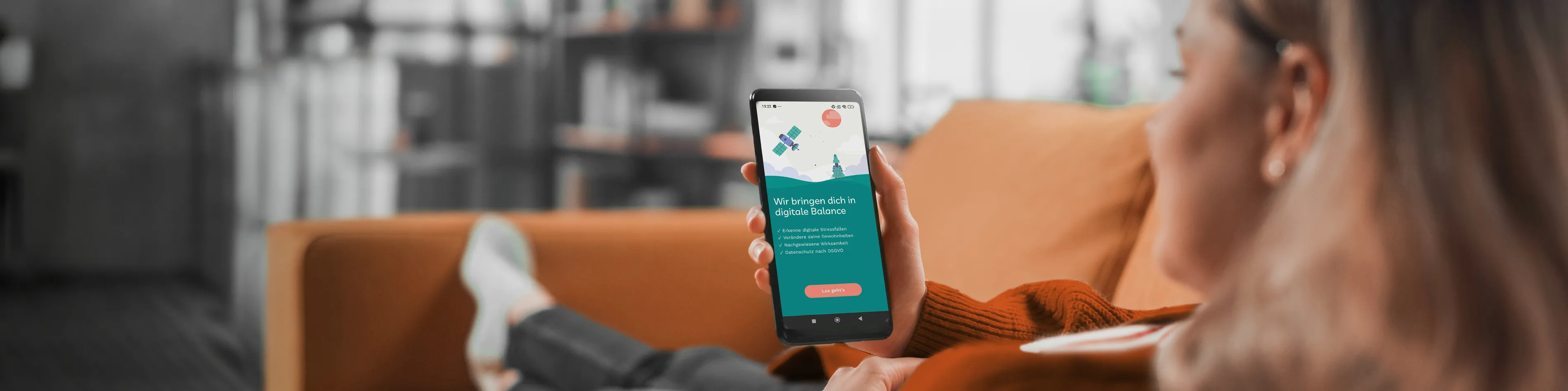 Eine Frau liegt entspannt auf dem Sofa und schaut sich über ihr Smartphone die Detoxi-App an. | VIACTIV Krankenkasse