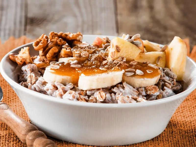 Eine Portion Porridge in einer weißen Schale, garniert mit Banane, Nüssen und Honig. | VIACTIV Krankenkasse