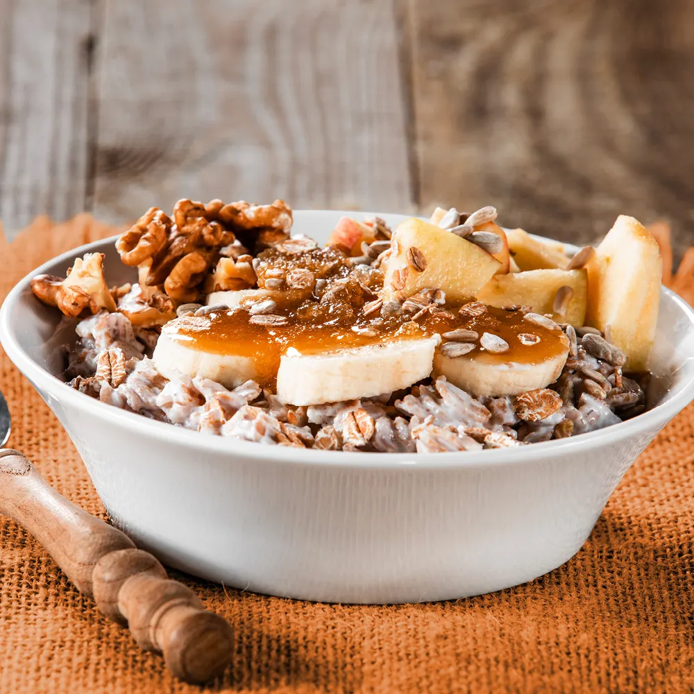 Eine Portion Porridge in einer weißen Schale, garniert mit Banane, Nüssen und Honig. | VIACTIV Krankenkasse