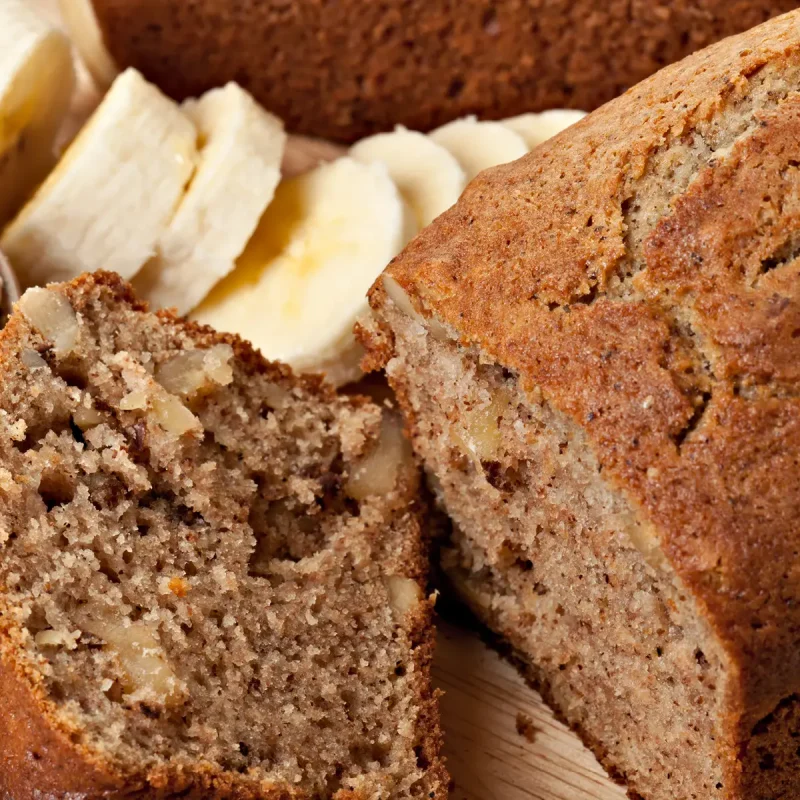 Bananenbrot zusammen mit frischen Bananenscheiben auf einem Holzbrett. | VIACTIV Krankenkasse
