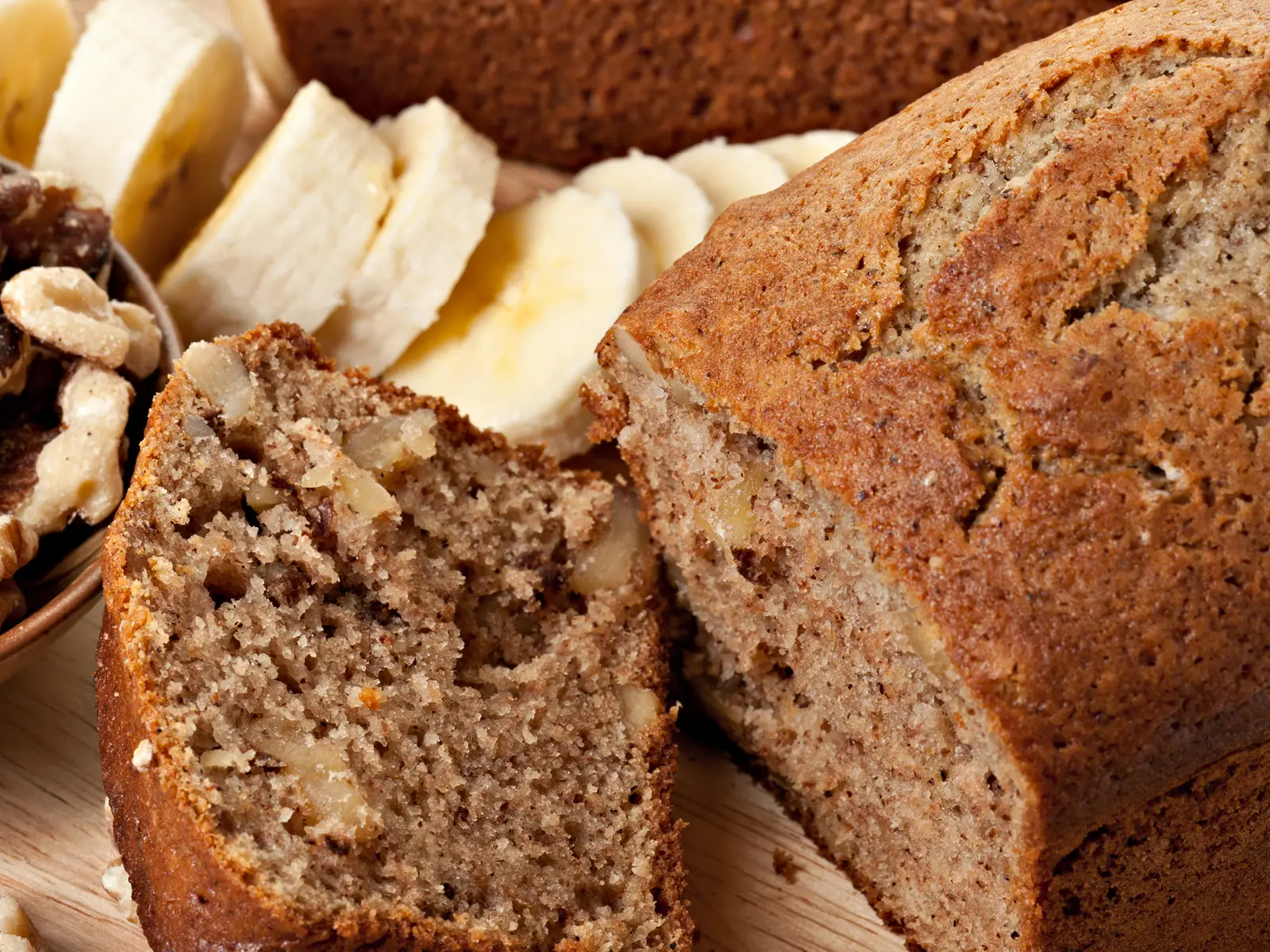 Bananenbrot zusammen mit frischen Bananenscheiben auf einem Holzbrett. | VIACTIV Krankenkasse