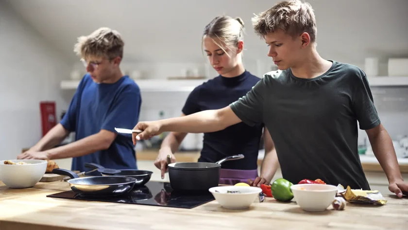 Auf dem Foto sind drei Jugendliche gemeinsam am kochen. Im Vordergrund ist ein Herd mit Töpfen und Pfannen zu sehen. | VIACTIV Krankenkasse