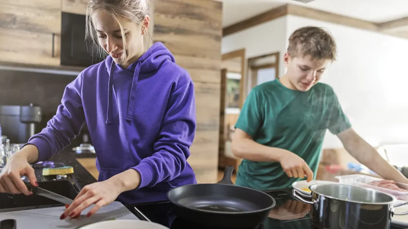 Zwei Jugendliche, ein Junge und ein Mädchen, kochen gemeinsam. Das Mädchen schneidet gerade etwas Gemüse. | VIACTIV Krankenkasse