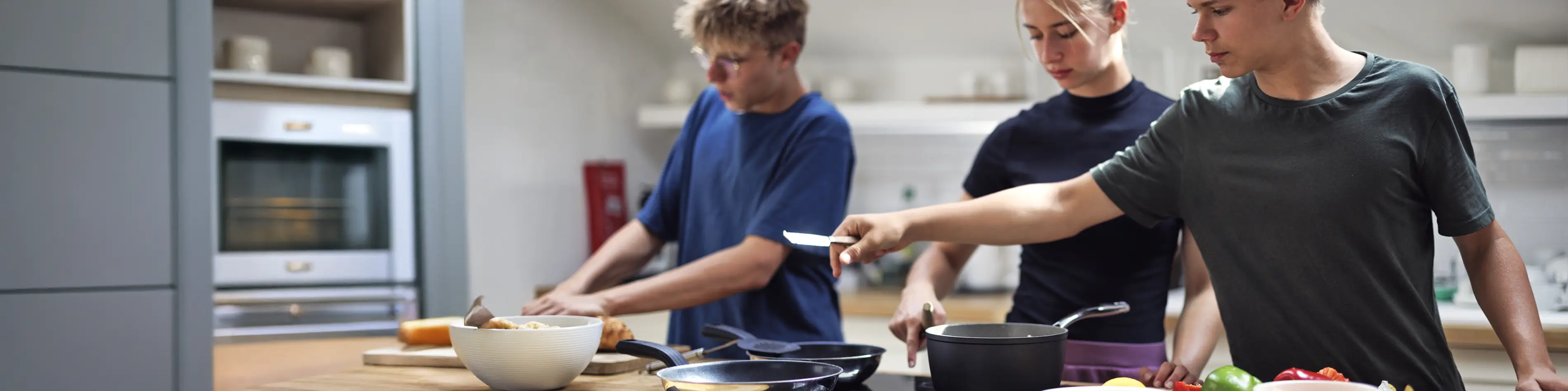 Auf dem Foto sind drei Jugendliche gemeinsam am kochen. Im Vordergrund ist ein Herd mit Töpfen und Pfannen zu sehen. | VIACTIV Krankenkasse