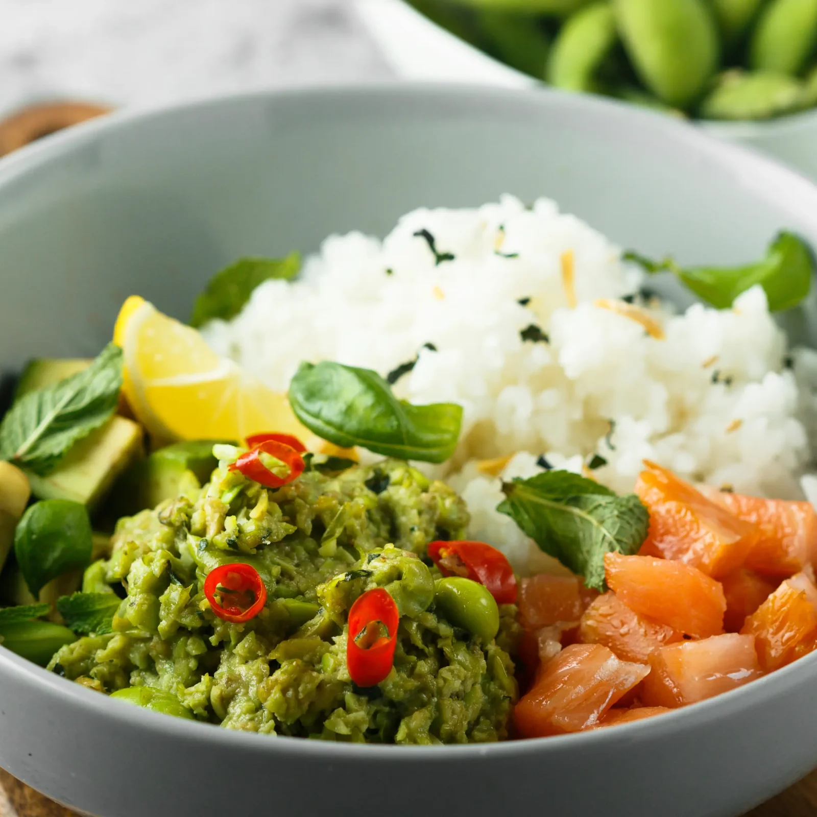 Eine Bowl aus Reis, Lachs und Avocadocreme garniert mit Kräutern in einer hellblauen Schale. | VIACTIV Krankenkasse