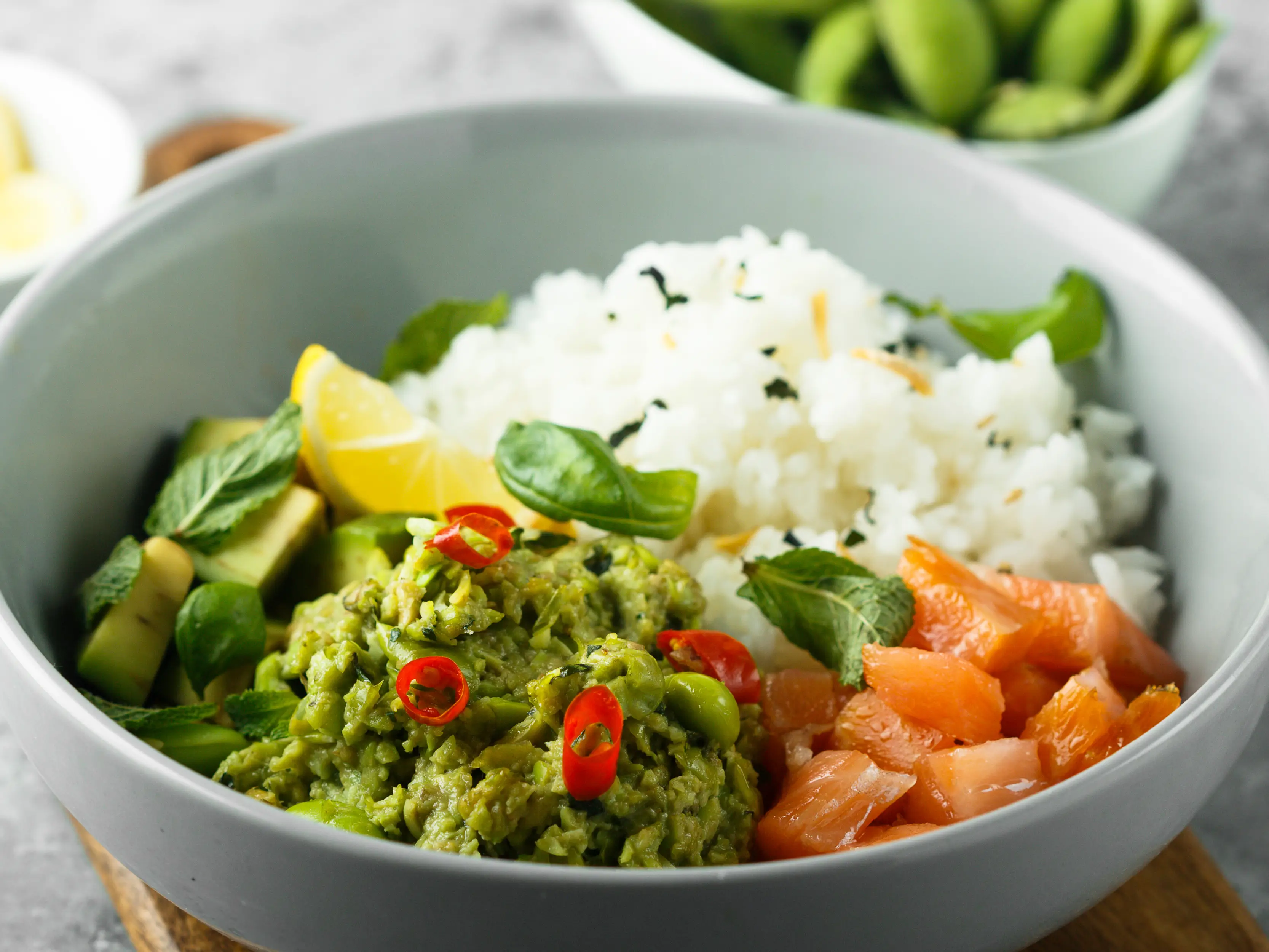 Eine Bowl aus Reis, Lachs und Avocadocreme garniert mit Kräutern in einer hellblauen Schale. | VIACTIV Krankenkasse