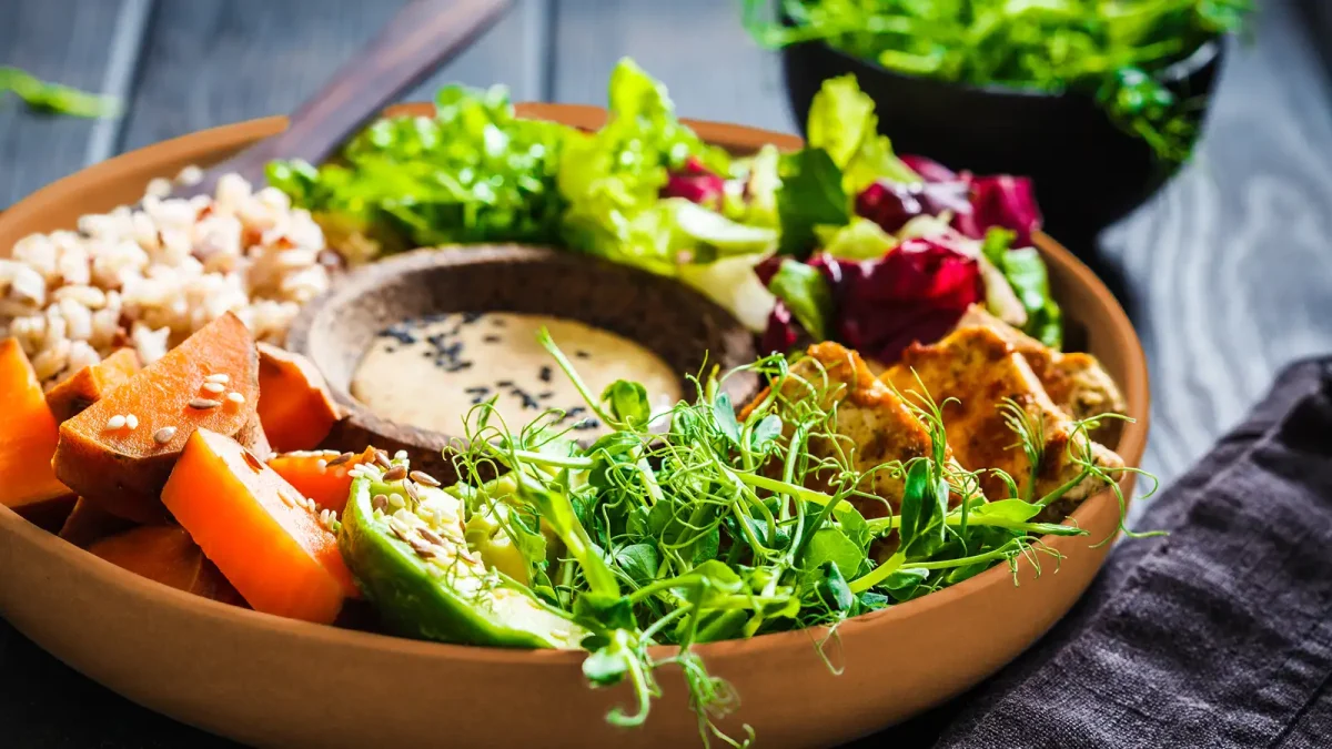 Ein tiefer Teller, auf dem Salat, Gemüse und Getreide mit einem Dressing angerichtet ist. | VIACTIV Krankenkasse