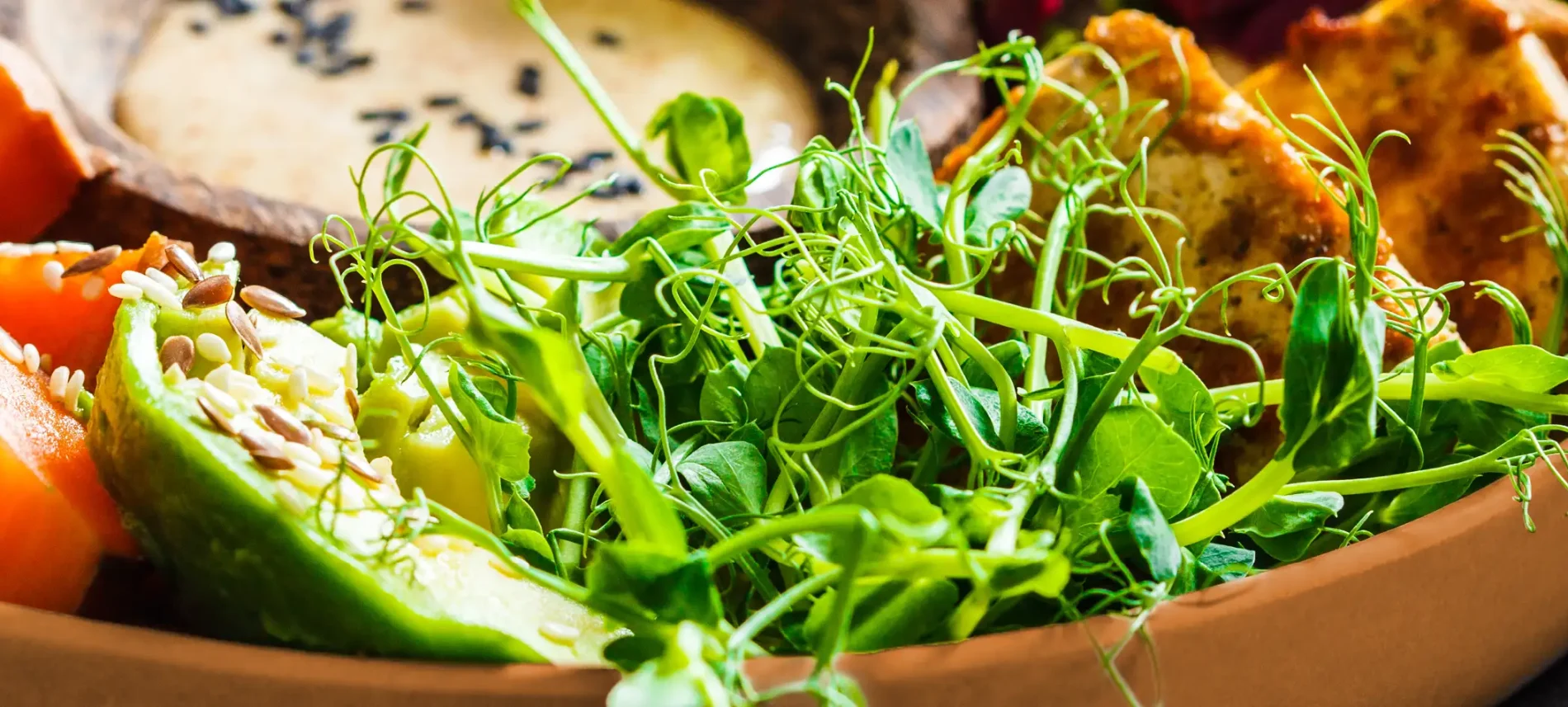 Ein tiefer Teller, auf dem Salat, Gemüse und Getreide mit einem Dressing angerichtet ist. | VIACTIV Krankenkasse