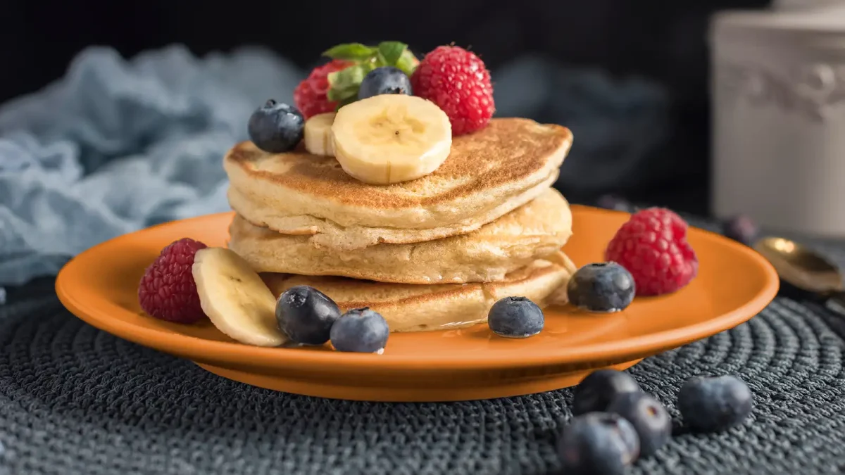 Ein orangener Teller auf dem Pfannkuchen und frisches Obst angerichtet sind. | VIACTIV Krankenkasse