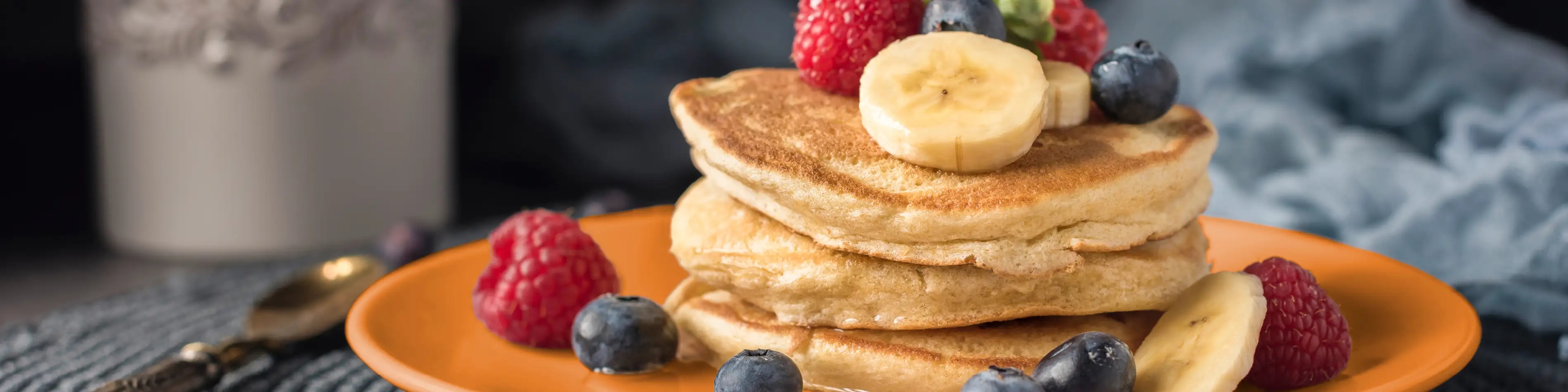 Ein orangener Teller auf dem Pfannkuchen und frisches Obst angerichtet sind. | VIACTIV Krankenkasse