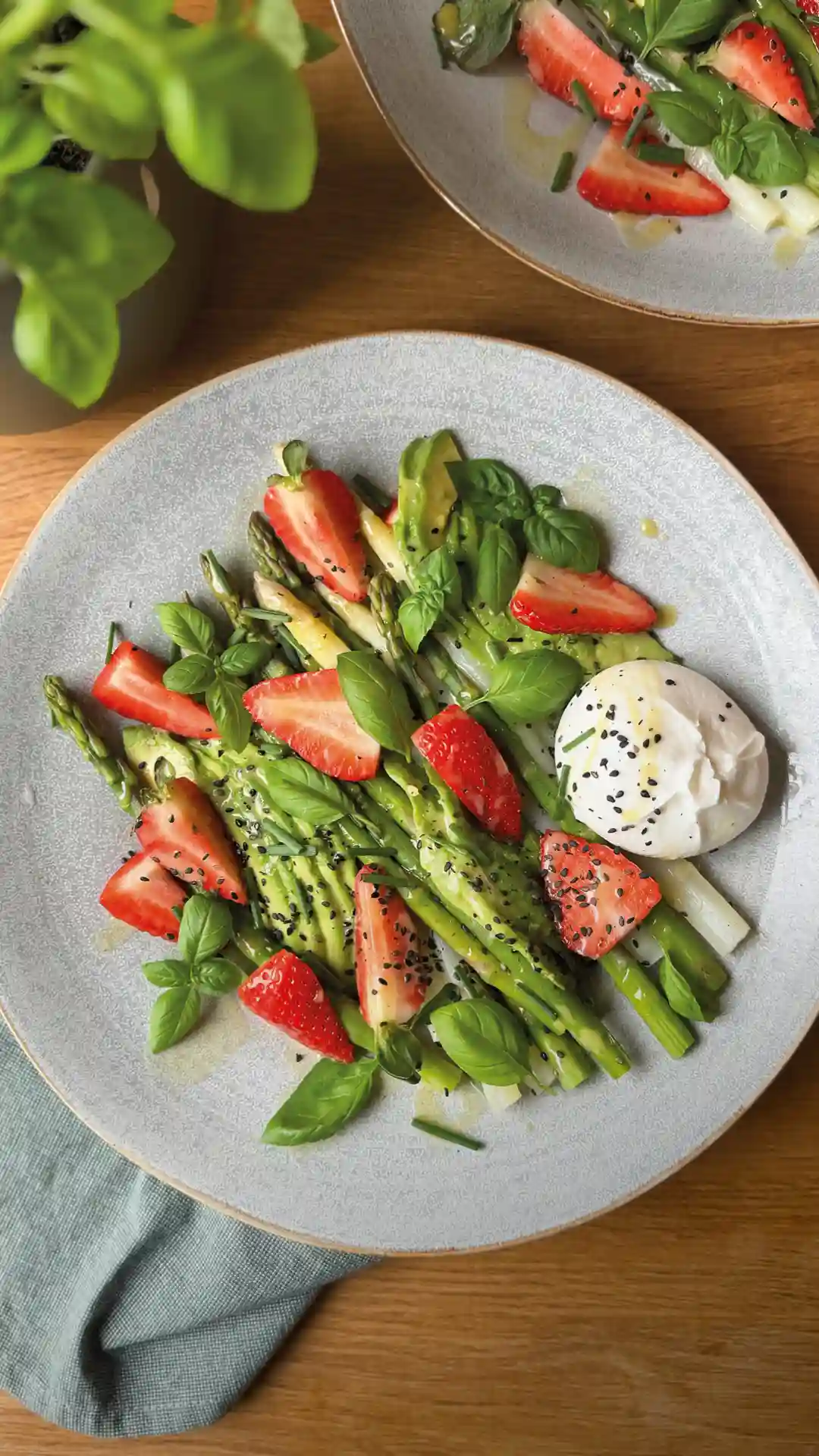 Ein Spargelsalat mit Burrata, garniert mit Erdbeeren auf einem hellgrauen Teller. | VIACTIV Krankenkasse