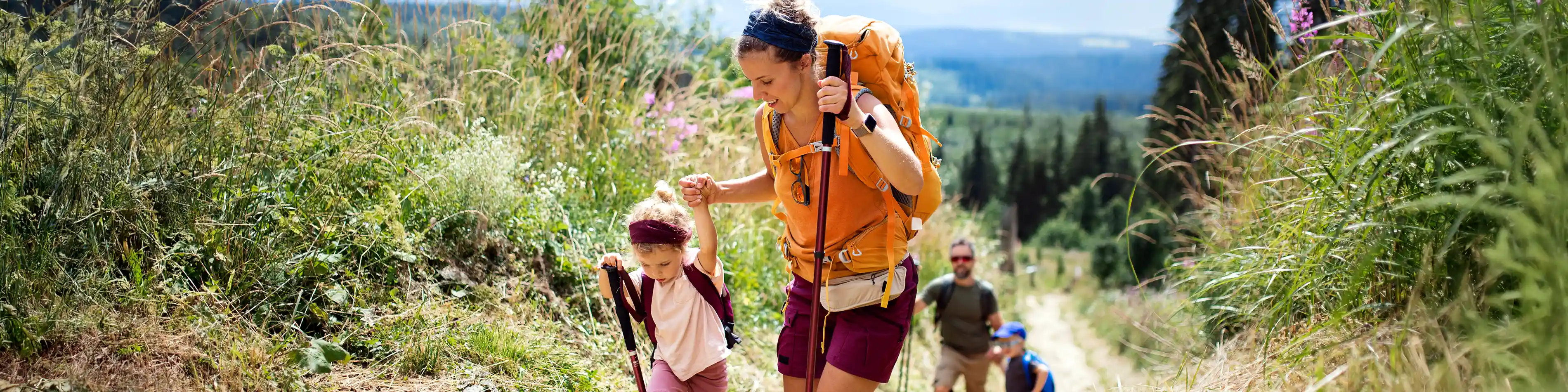 Eine vierköpfige Familie ist mit Wanderstöcken in der Natur unterwegs. | VIACTIV Krankenkasse