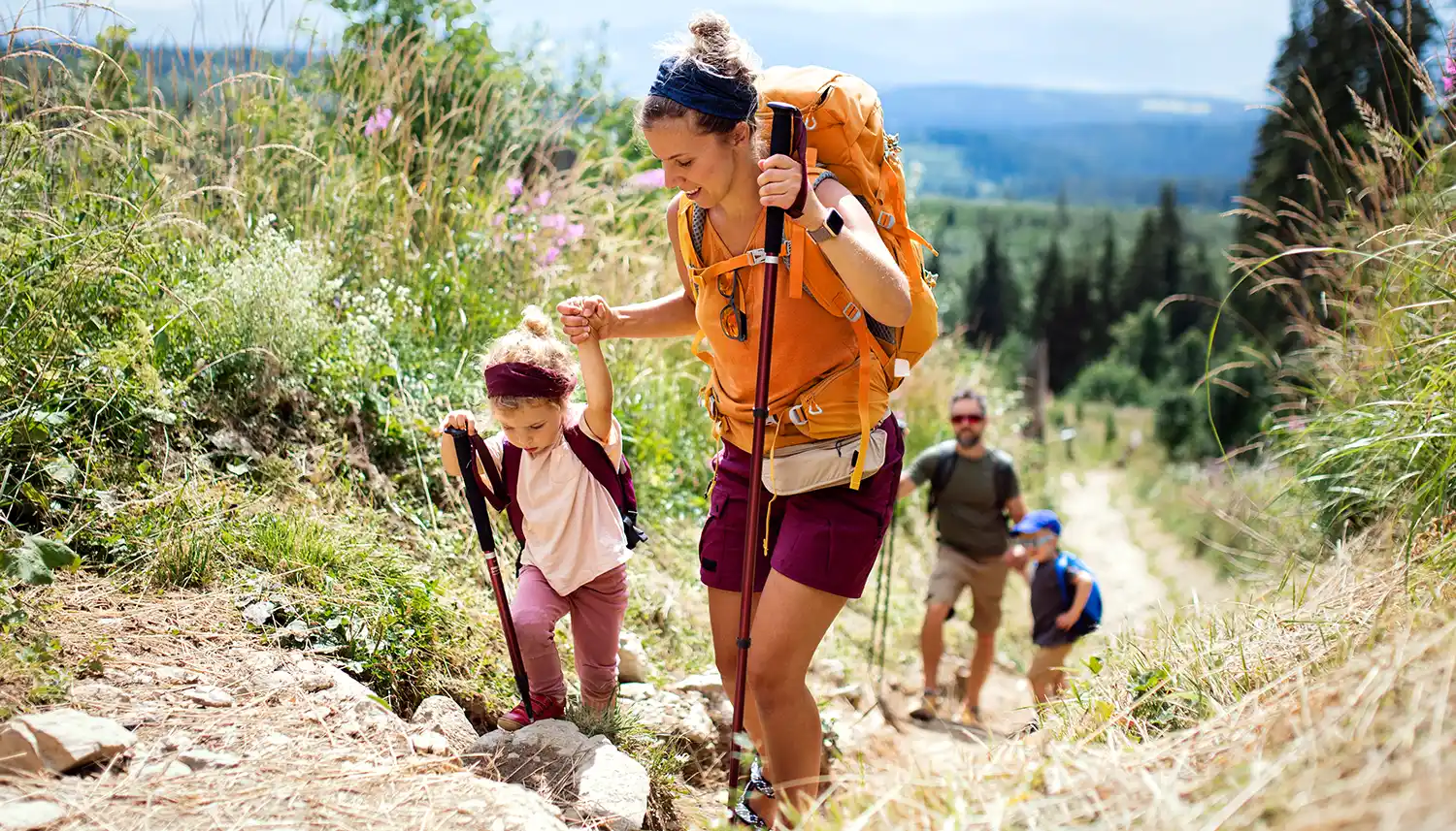 Eine vierköpfige Familie ist mit Wanderstöcken in der Natur unterwegs. | VIACTIV Krankenkasse
