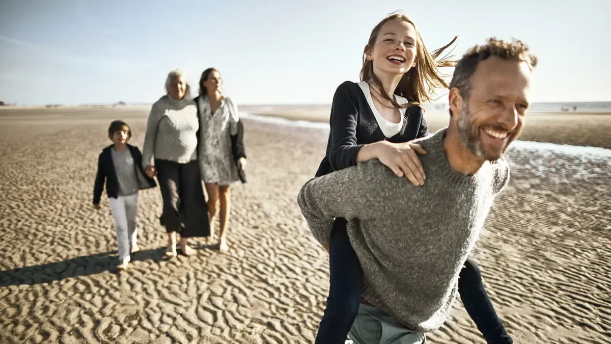 Eine Familie spielt glücklich am Strand. Sie sind familienversichert und bekommen Bonus von ihrer Krankenkasse für einen aktiven Lebensstil. | VIACTIV Krankenkasse