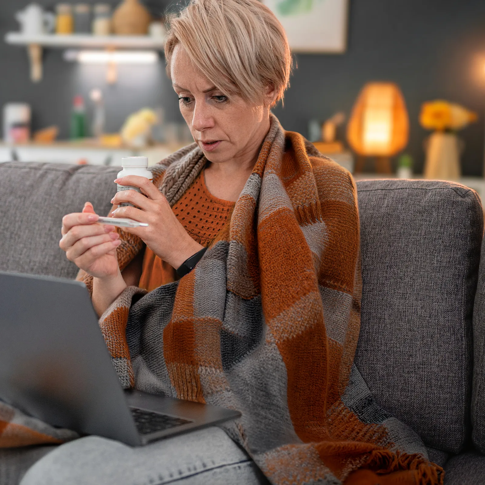 Eine Frau sitzt auf dem Sofa und hat einen Laptop auf ihren Beinen liegen. Sie schaut parallel auf einen Schnelltest. | VIACTIV Krankenkasse