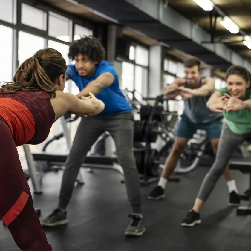 Vier Personen machen gemeinsam in einem Fitnessstudio eine Sportübung, bei der sich sich mit gestreckten Armen vorneüber beugen. | VIACTIV Krankenkasse