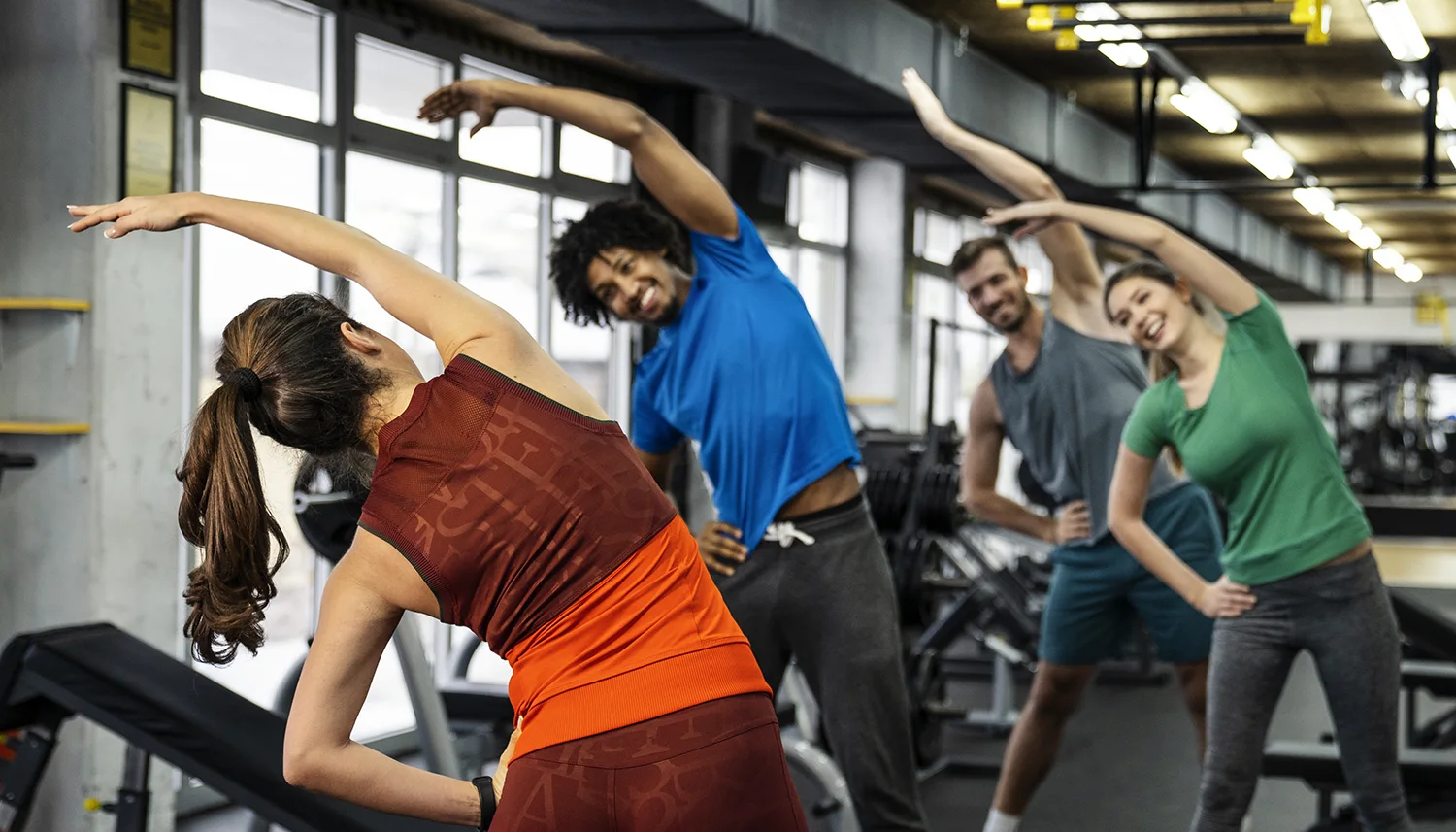 Vier Personen stehen im Fitnessstudio und machen gemeinsam die Übung Seitbeuger. | VIACTIV Krankenkasse