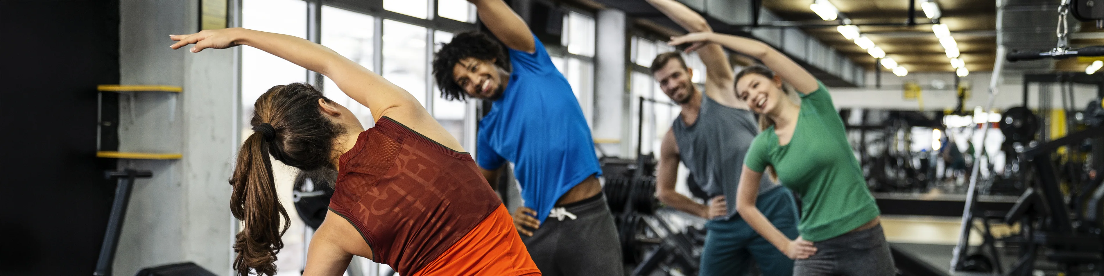Vier Personen stehen im Fitnessstudio und machen gemeinsam die Übung Seitbeuger. | VIACTIV Krankenkasse