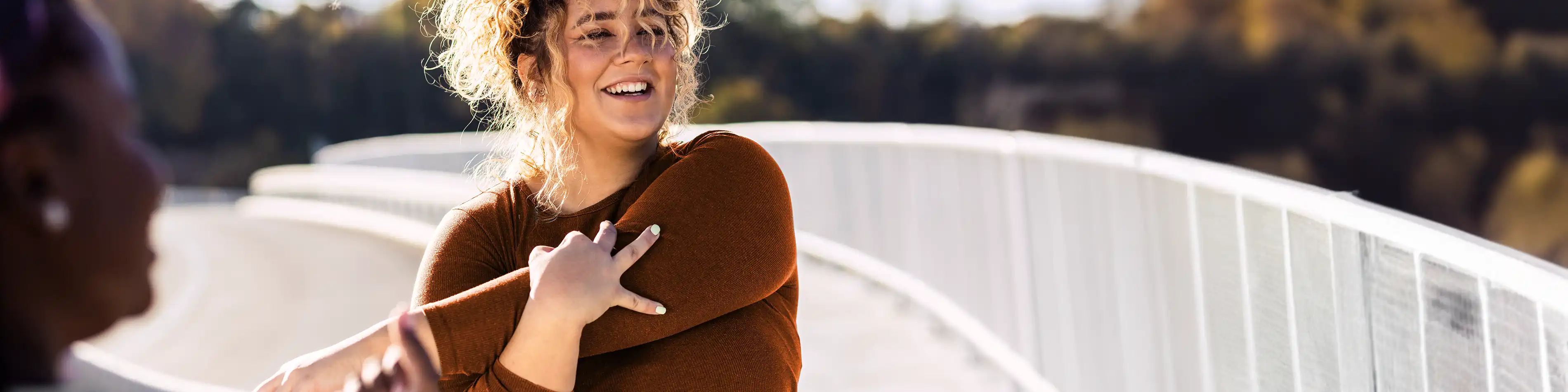 Eine junge Frau dehnt ihren linken Arm. Sie trägt Sportkleidung und lächelt. | VIACTIV Krankenkasse