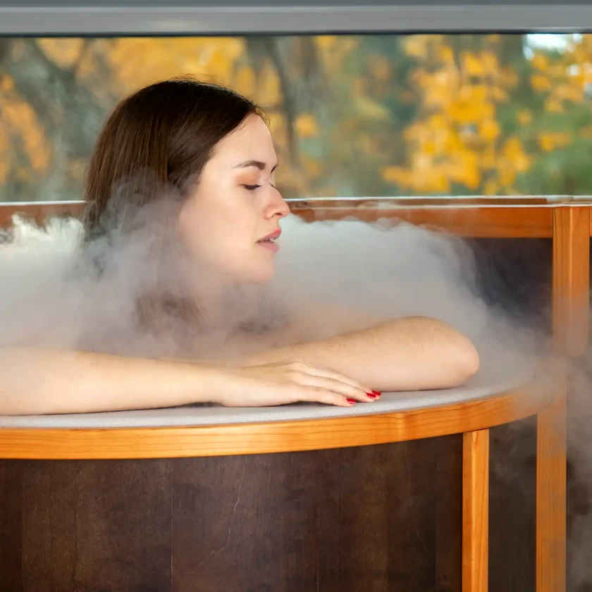 Eine junge Frau sitzt in einer kleinen offenen Sauna. Um ihren Kopf herum ist Dampf zu sehen. | VIACTIV Krankenkasse