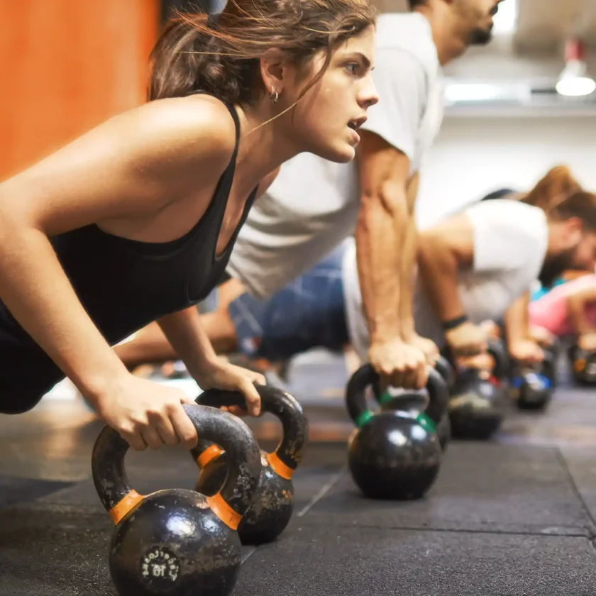 Eine Gruppe trainiert mit Kettlebells im Fitnessstudio. Die Frau im Vordergrund setzt zum Liegestütz auf den Kettlebells an. | VIACTIV Krankenkasse