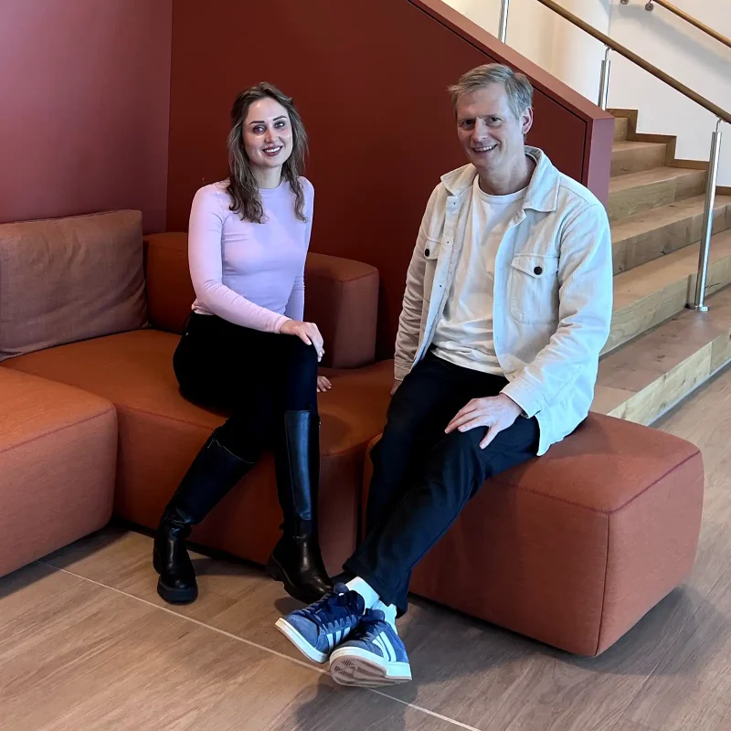 Die VIACTIV Mitarbeitenden Emma Seifert und Norbert Winzen aus dem BGM-Team sitzen auf einem Sofa. | VIACTIV Krankenkasse