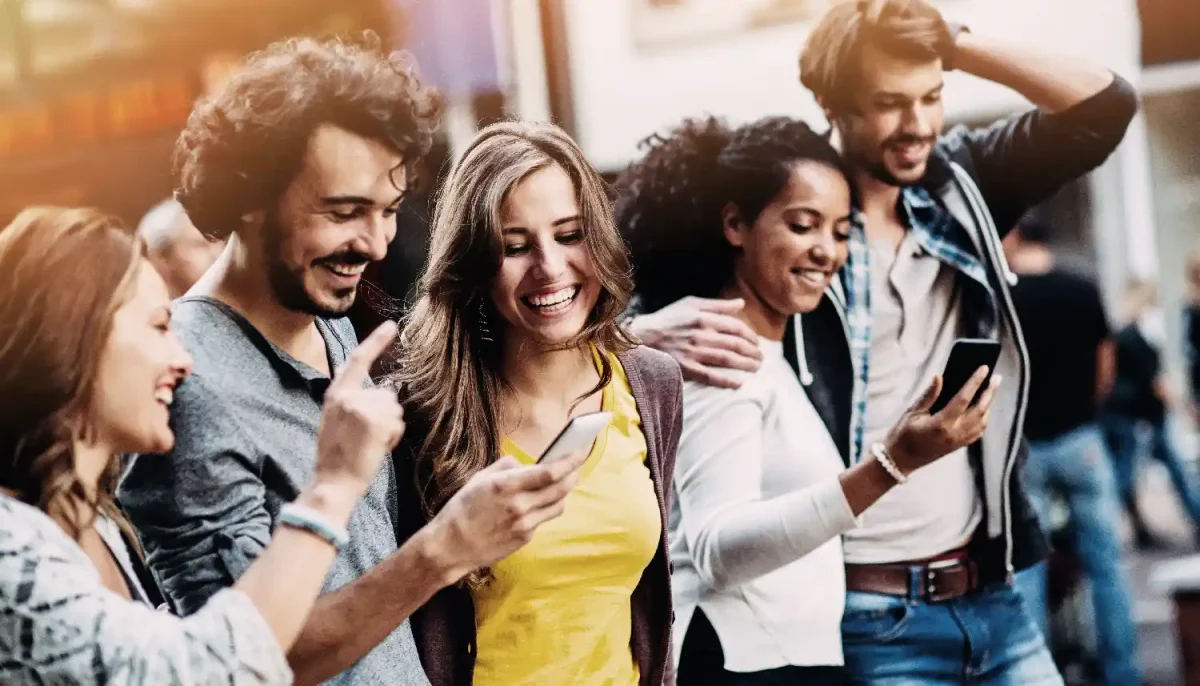 Eine Gruppe junger Menschen steht auf der Straße. Sie schauen gemeinsam auf ein Smartphone, lachen und surfen durch Instagram. | VIACTIV Krankenkasse