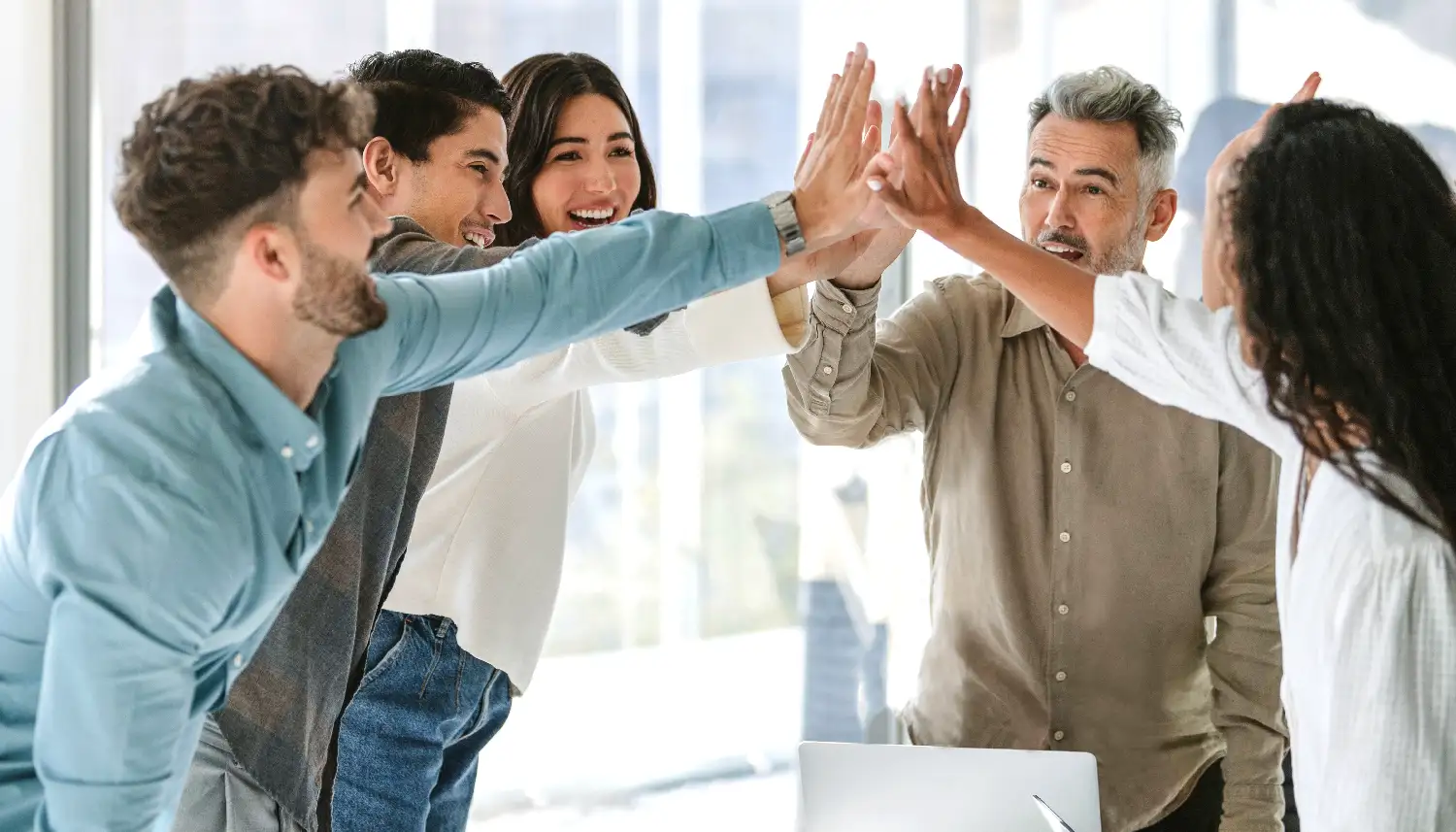 Fünf Personen im Business-Look geben sich ein High Five als Zeichen von Teamwork. | VIACTIV Krankenkasse