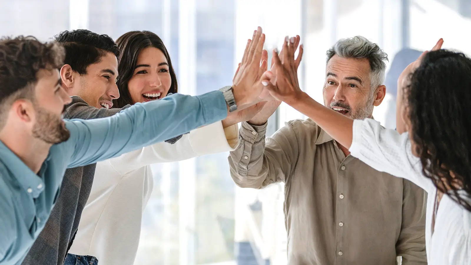 Fünf Personen im Business-Look geben sich ein High Five als Zeichen von Teamwork. | VIACTIV Krankenkasse