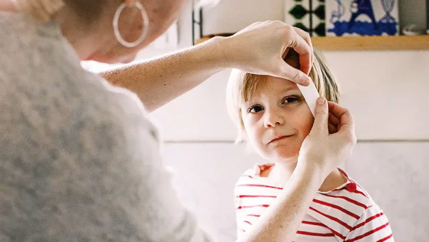 Ein kleines Kind wird von der Großmutter mit einem Pflaster am Kopf verarztet. | VIACTIV Krankenkasse