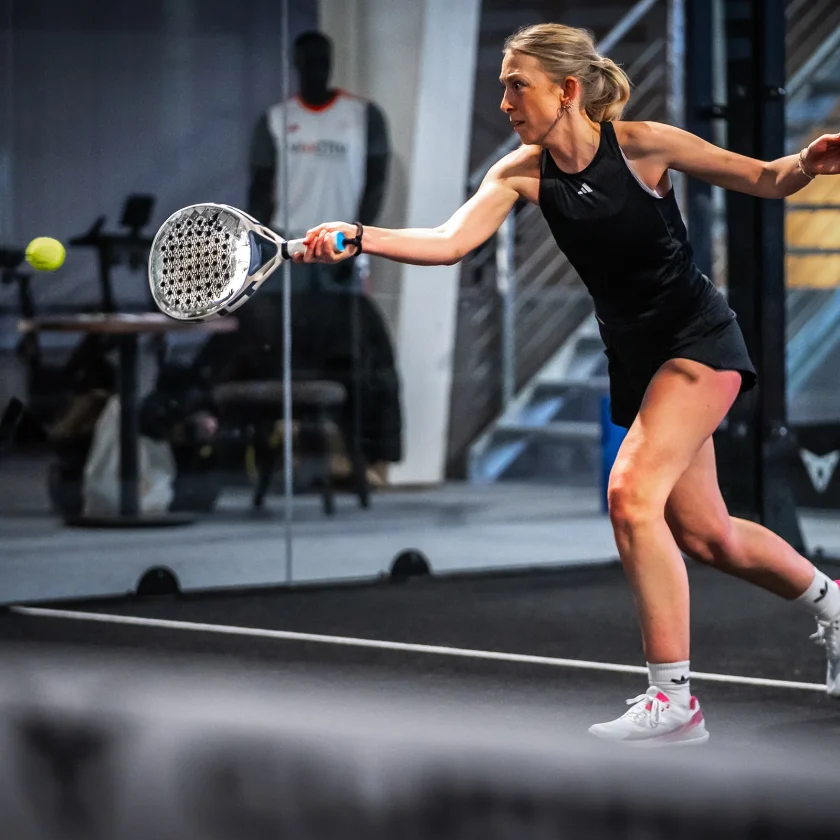 Eine Frau beim Padel-Tennis spielen auf einem Tennisplatz, die einen Schlag ausführt. | VIACTIV Krankenkasse