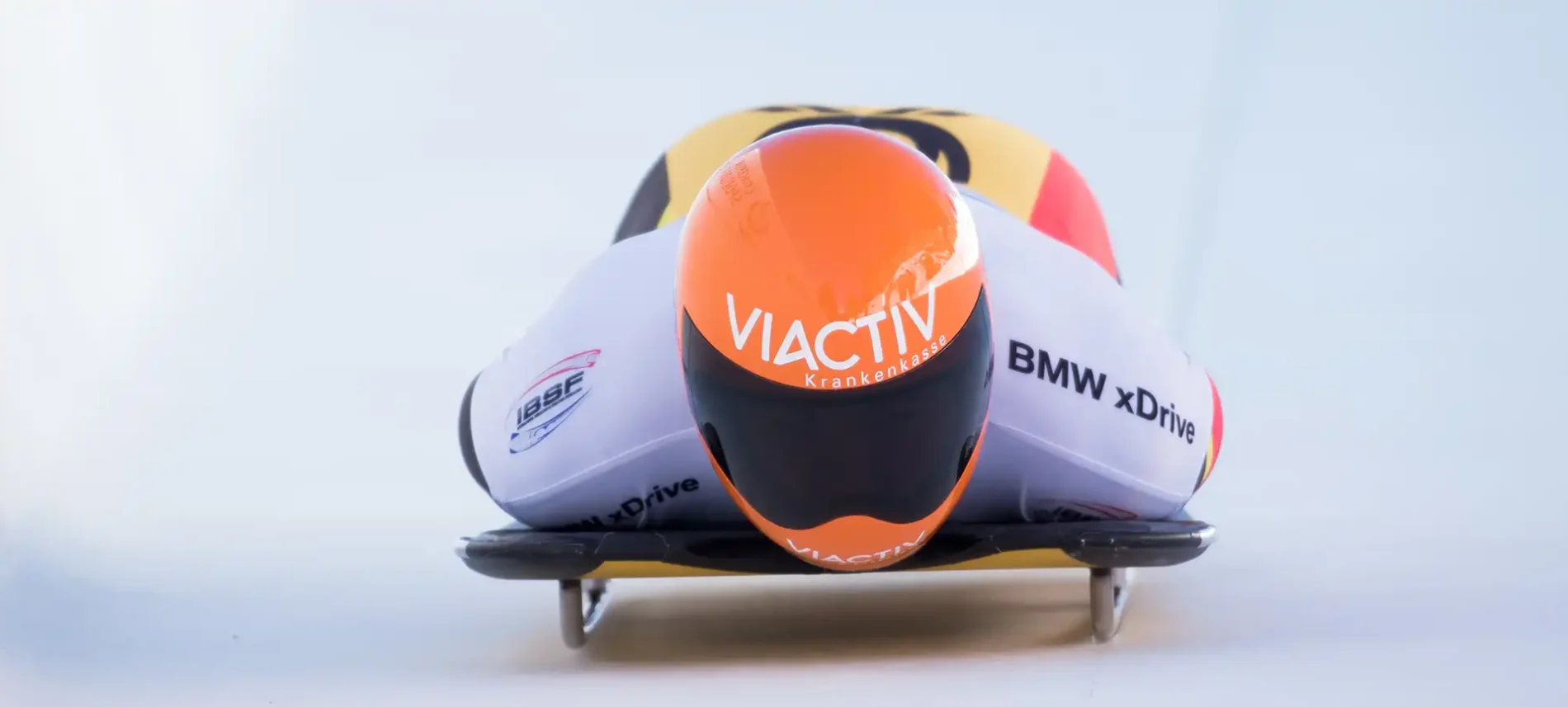Der Skeleton-Pilot Felix Keisinger fährt bäuchlings auf dem Rodelschlitten durch den Eiskanal. Er trägt den orangenen VIACTIV-Helm. | VIACTIV Krankenkasse