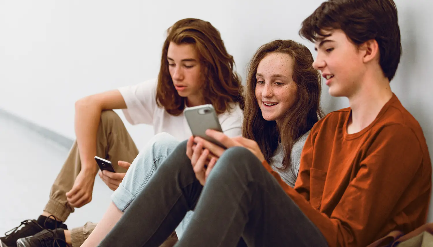 Drei Jugendliche sitzen nebeneinander auf dem Boden und schauen in ihre Handys. | VIACTIV Krankenkasse