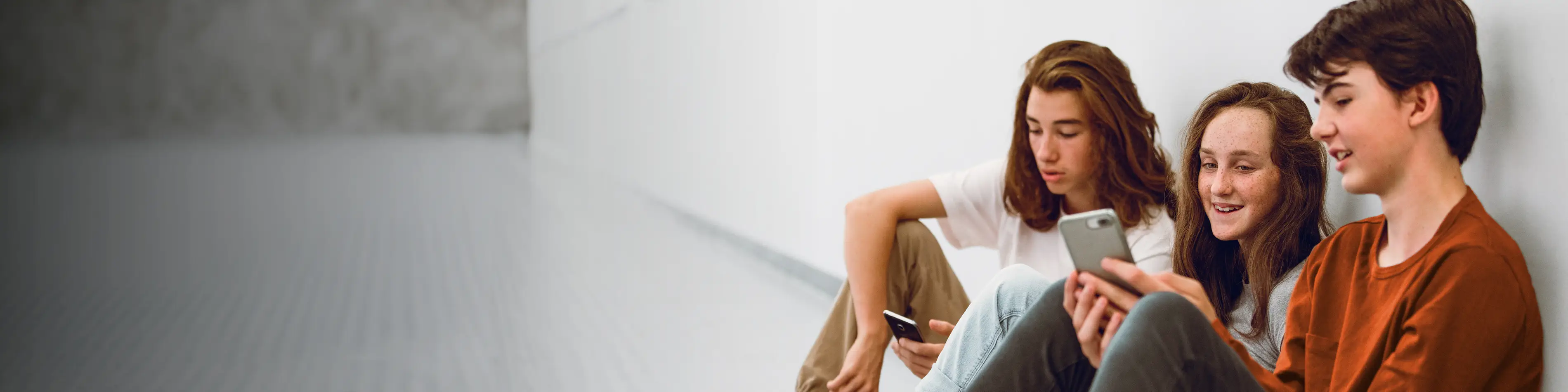 Drei Jugendliche sitzen nebeneinander auf dem Boden und schauen in ihre Handys. | VIACTIV Krankenkasse