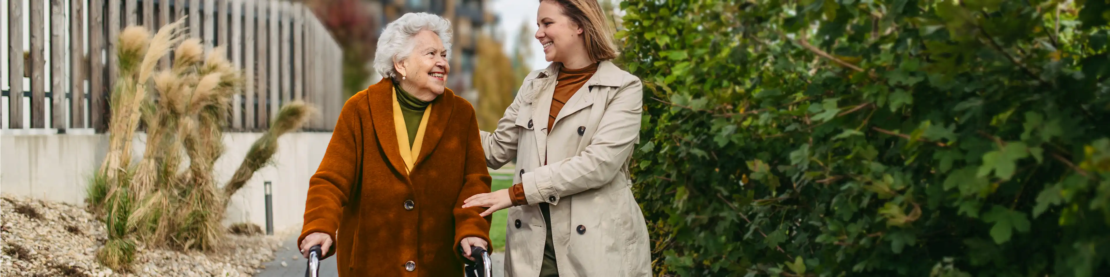 Eine ältere Frau mit einem Rollator wird auf einem Spaziergang begleitet von einer jüngeren Frau. | VIACTIV Krankenkasse