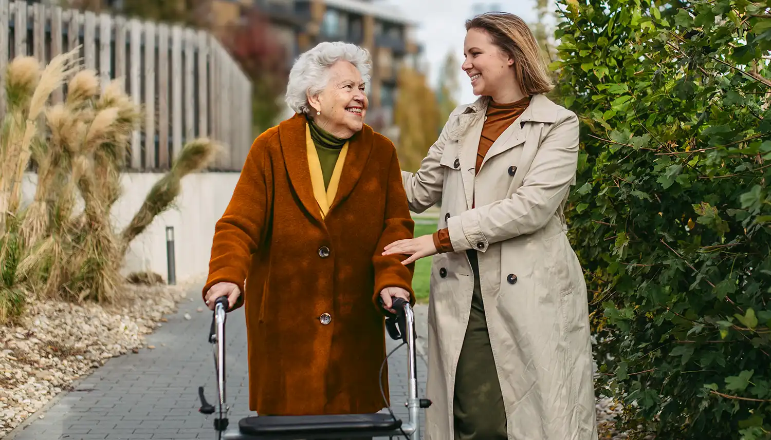 Eine ältere Frau mit einem Rollator wird auf einem Spaziergang begleitet von einer jüngeren Frau. | VIACTIV Krankenkasse