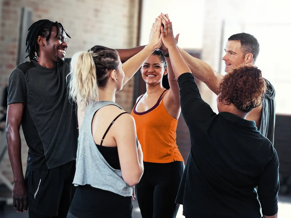 Eine Gruppe junger Menschen geben sich ein High Five in der Sporthalle. | VIACTIV Krankenkasse