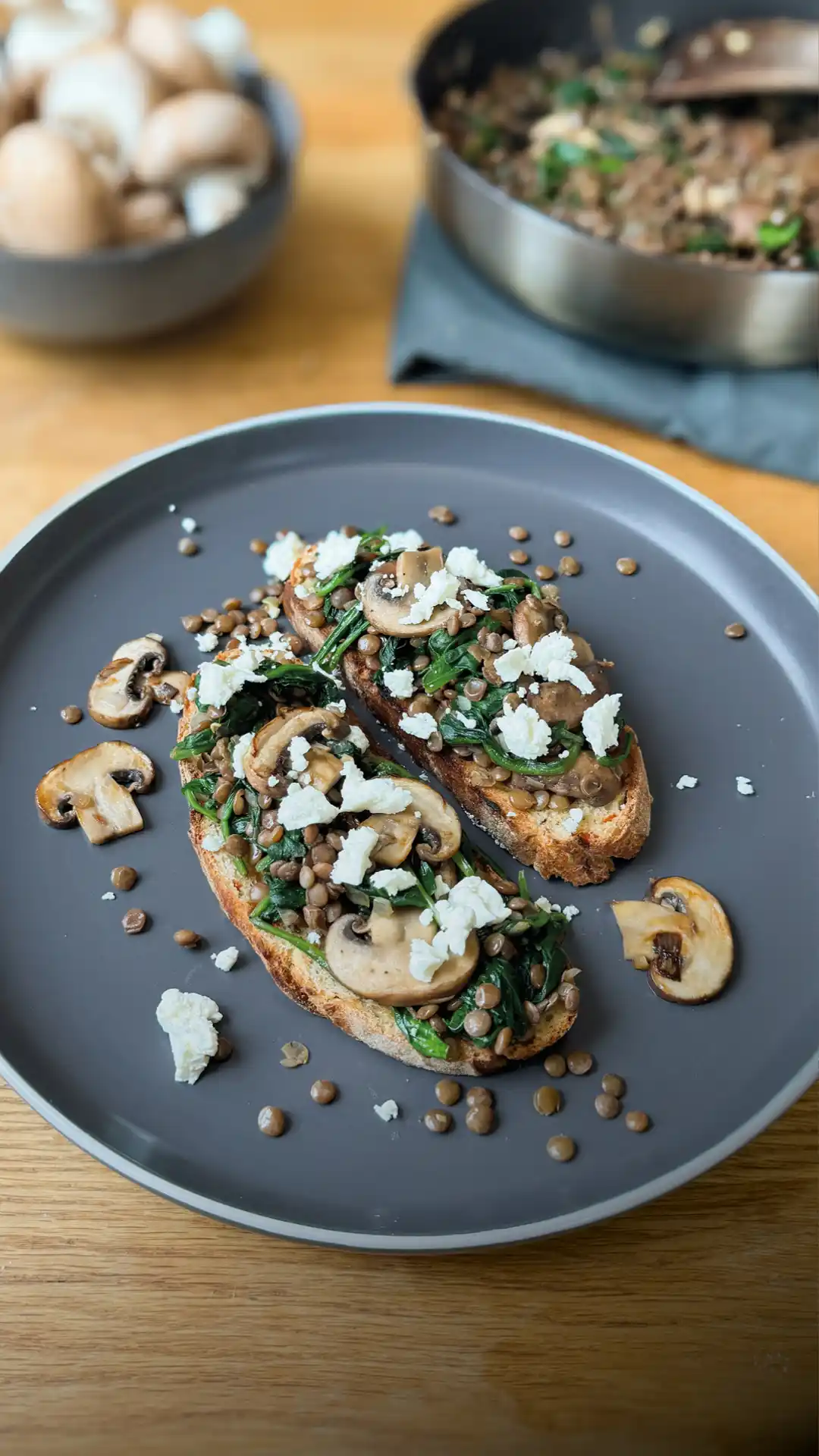 Zwei Scheiben Brot belegt mit Linsenbruschetta und Champignons auf einem dunklen Teller | VIACTIV Krankenkasse