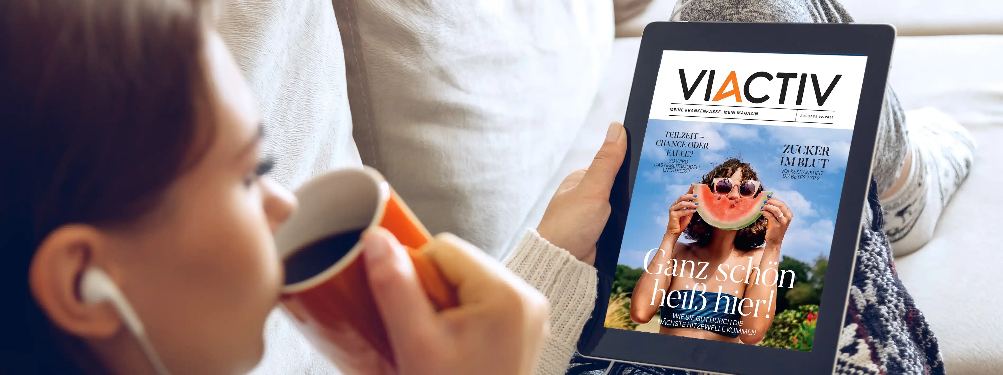 Eine junge Frau sitzt auf der Couch und liest das VIACTIV Sommermagazin auf einem Tablet. Sie trinkt dabei einen Kaffee. | VIACTIV Krankenkasse