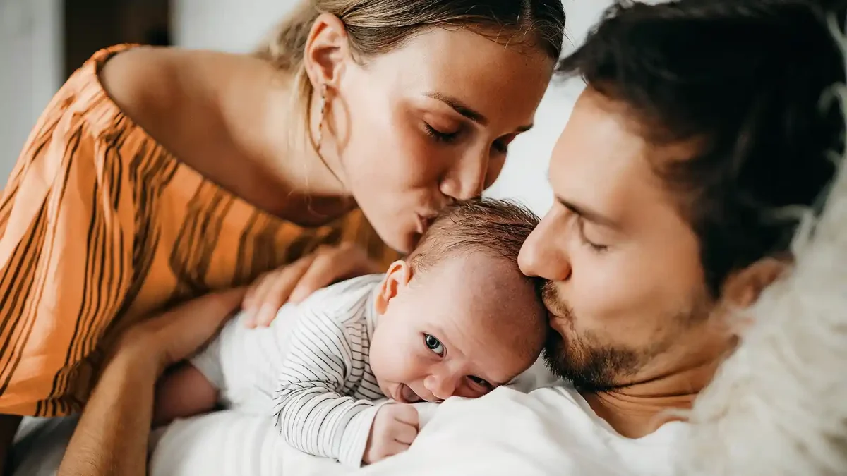 Eine Frau und ein Mann haben ein Baby in ihrer Mitte und beide küssen es auf den Kopf. | VIACTIV Krankenkasse