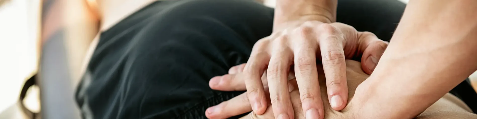 Ein Therapeut übt im Rahmen einer Osteopathiebehandlung mit seinen Händen Druck auf den unteren Rücken eines Patienten aus. | VIACTIV Krankenkasse