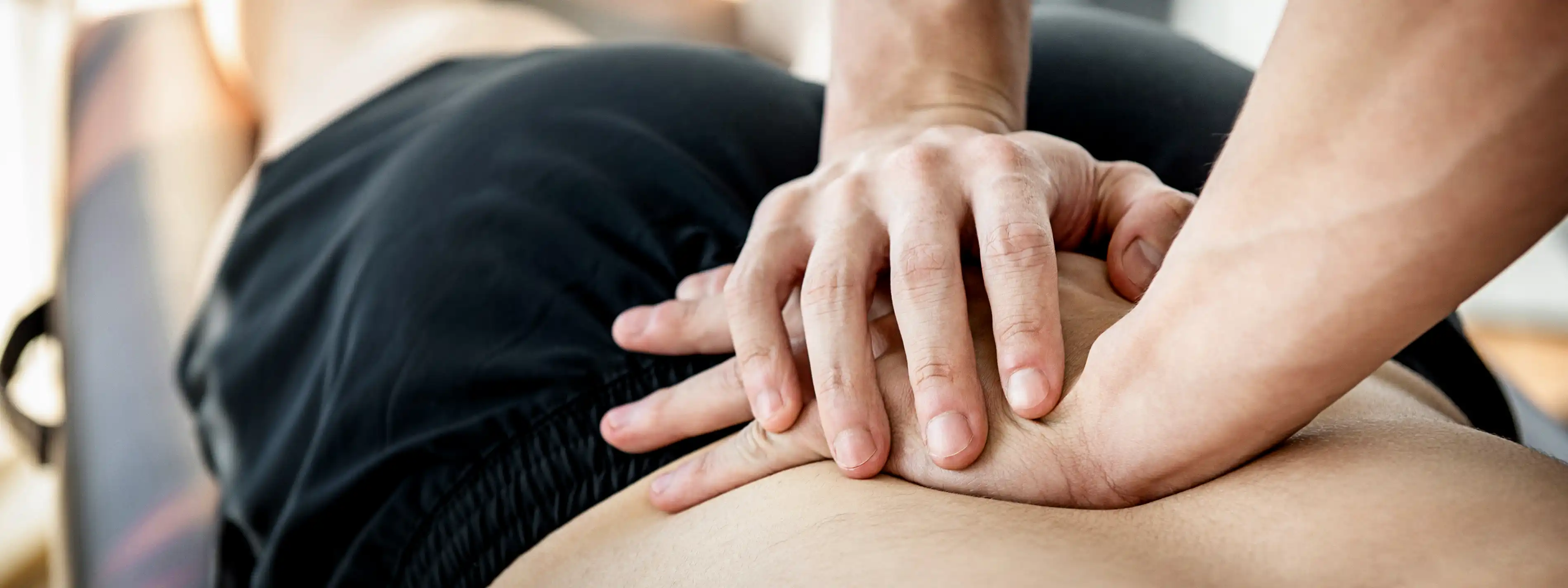 Ein Therapeut übt im Rahmen einer Osteopathiebehandlung mit seinen Händen Druck auf den unteren Rücken eines Patienten aus. | VIACTIV Krankenkasse