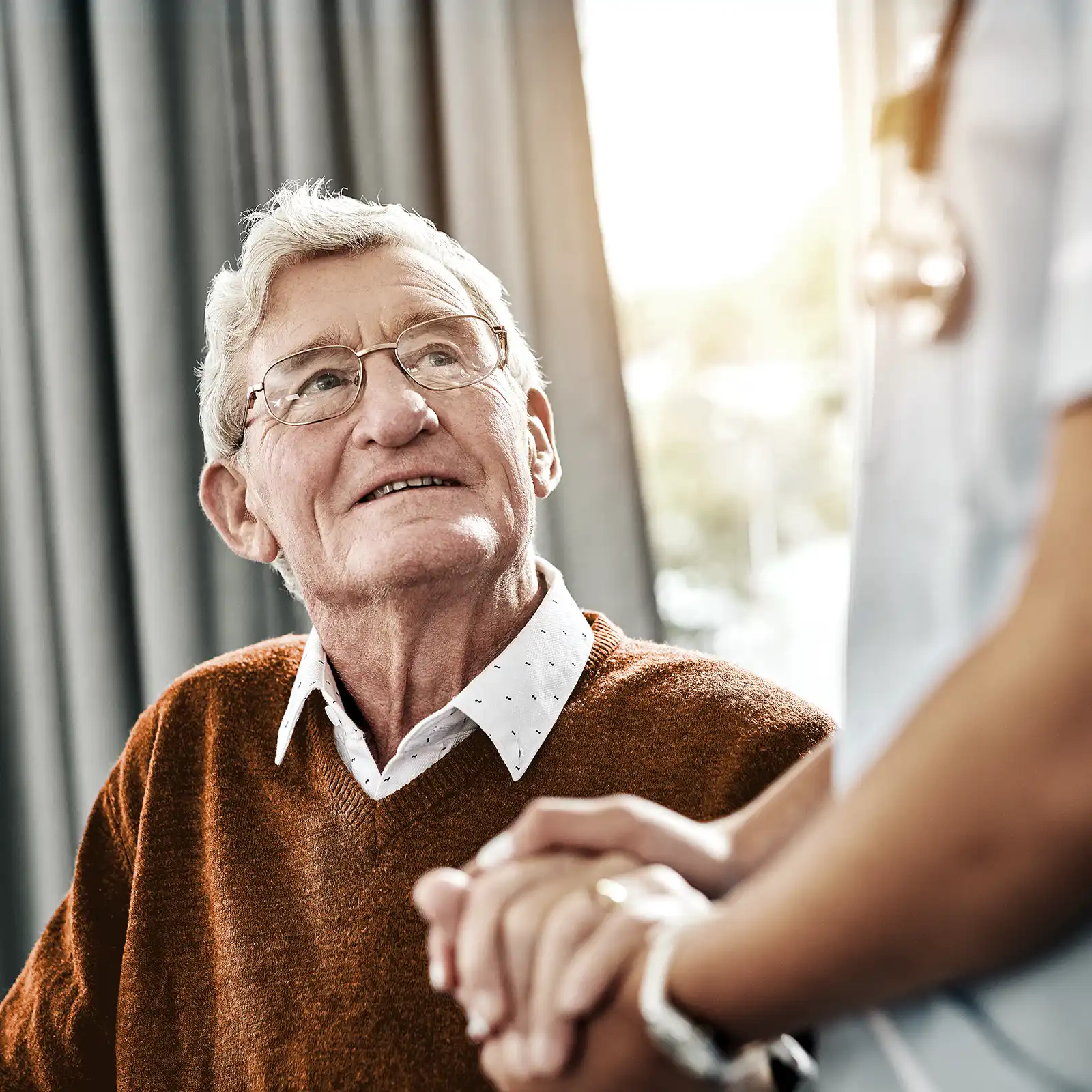 Ein älterer Mann blickt zur Pflegekraft auf und sie hält seine Hand. | VIACTIV Krankenkasse